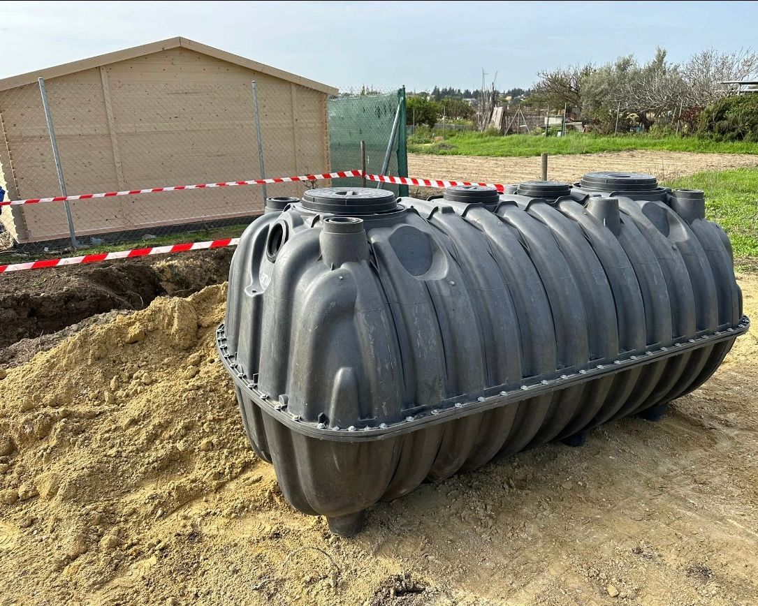 Un gran tanque séptico negro se encuentra en el suelo frente a un cobertizo de madera.