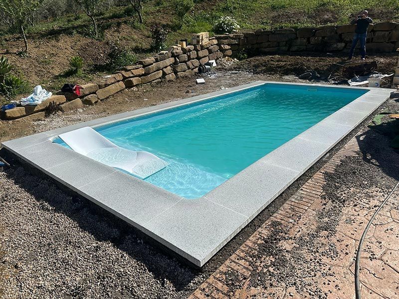 Piscina rectangular de agua azul y borde gris, en un entorno al aire libre.