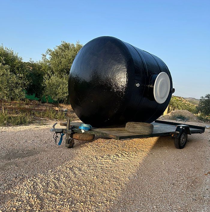 Tanque negro en un remolque en un entorno rural con cielo azul.