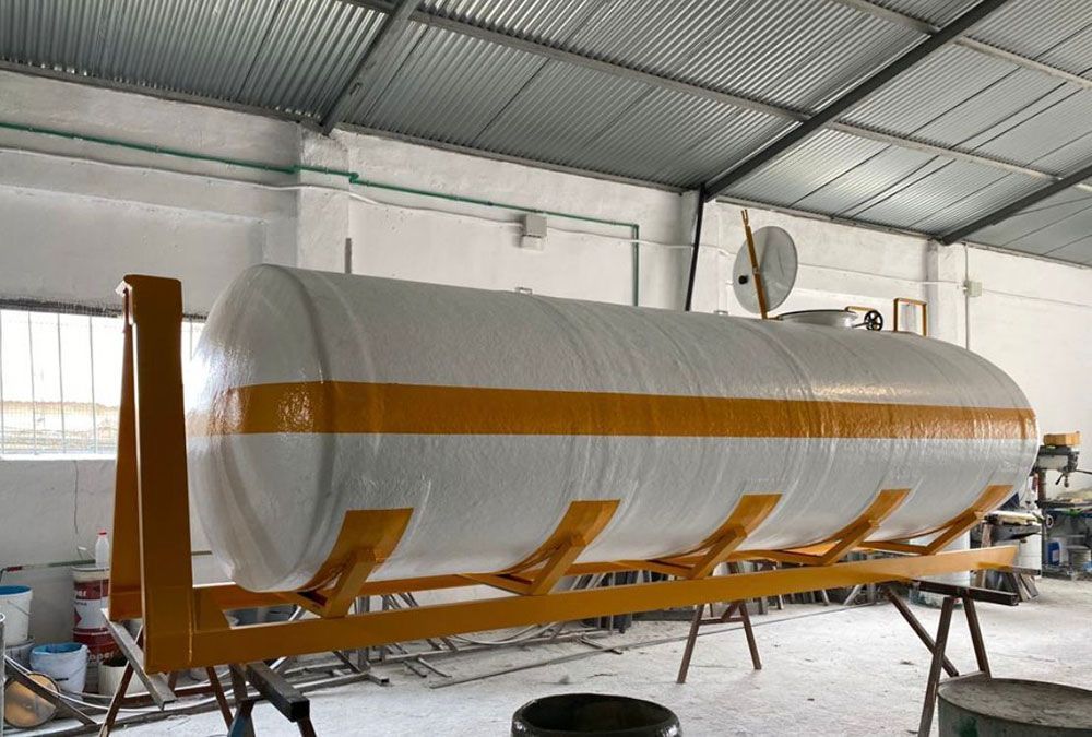 Gran tanque cilíndrico de color amarillo y blanco, envuelto en blanco, montado sobre un marco amarillo dentro de un edificio.