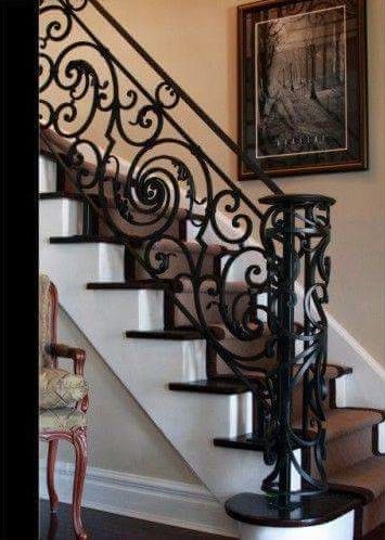 Escalera ornamentada de hierro forjado negro con escalones blancos y un cuadro enmarcado en la pared.