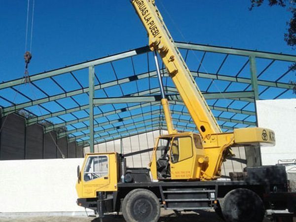Una grúa amarilla levanta vigas de acero dentro de la estructura de un almacén parcialmente construido.