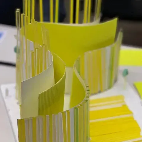 Escultura abstracta de papel amarillo con líneas verticales y formas curvas.