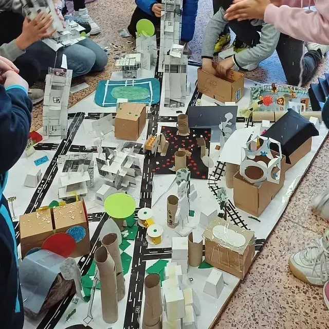 Niños rodeando una maqueta de ciudad de cartón, elaborada con materiales reciclados.