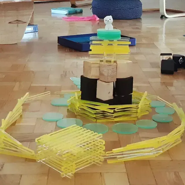 Una colorida torre de bloques y formas sobre un piso de madera, rodeada de piezas amarillas y verdes.