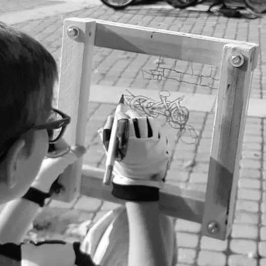 Persona dibujando una bicicleta a través de un marco de madera al aire libre.