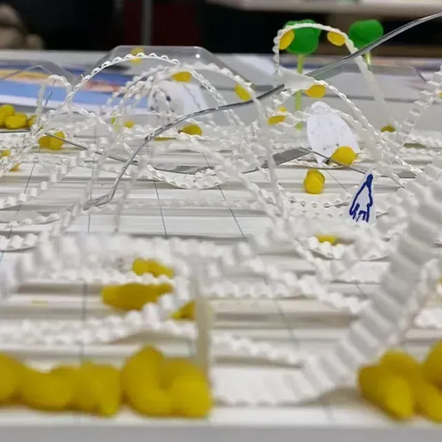 Primer plano de una maqueta arquitectónica blanca con acentos amarillos; arcos y estructuras lineales, sobre una superficie blanca.