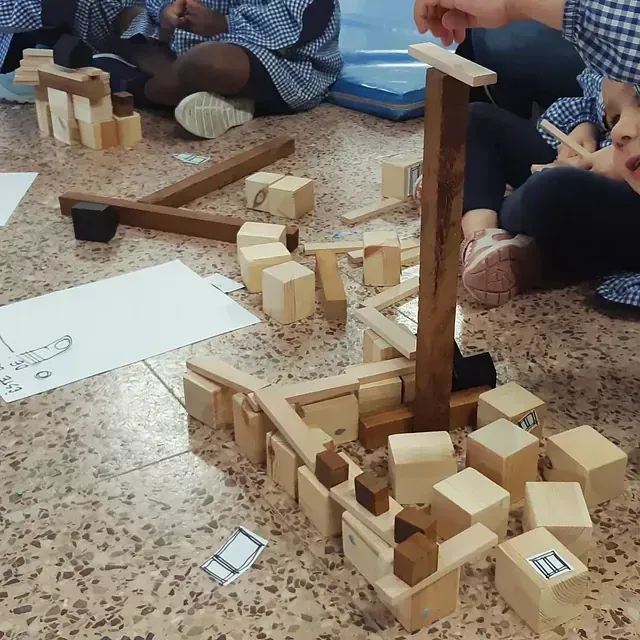 Niños construyendo con bloques de madera en un piso, construcción colaborativa de una estructura.