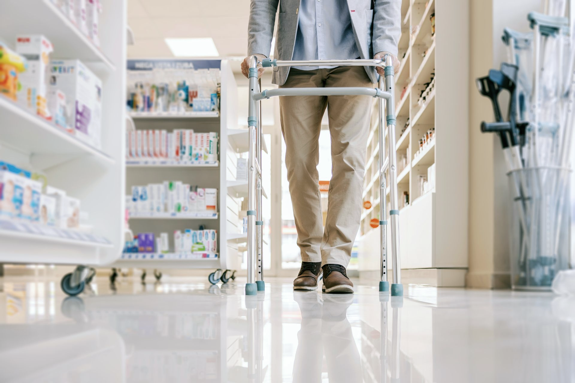 Une personne utilise un déambulateur métallique pour se déplacer dans une allée de pharmacie.