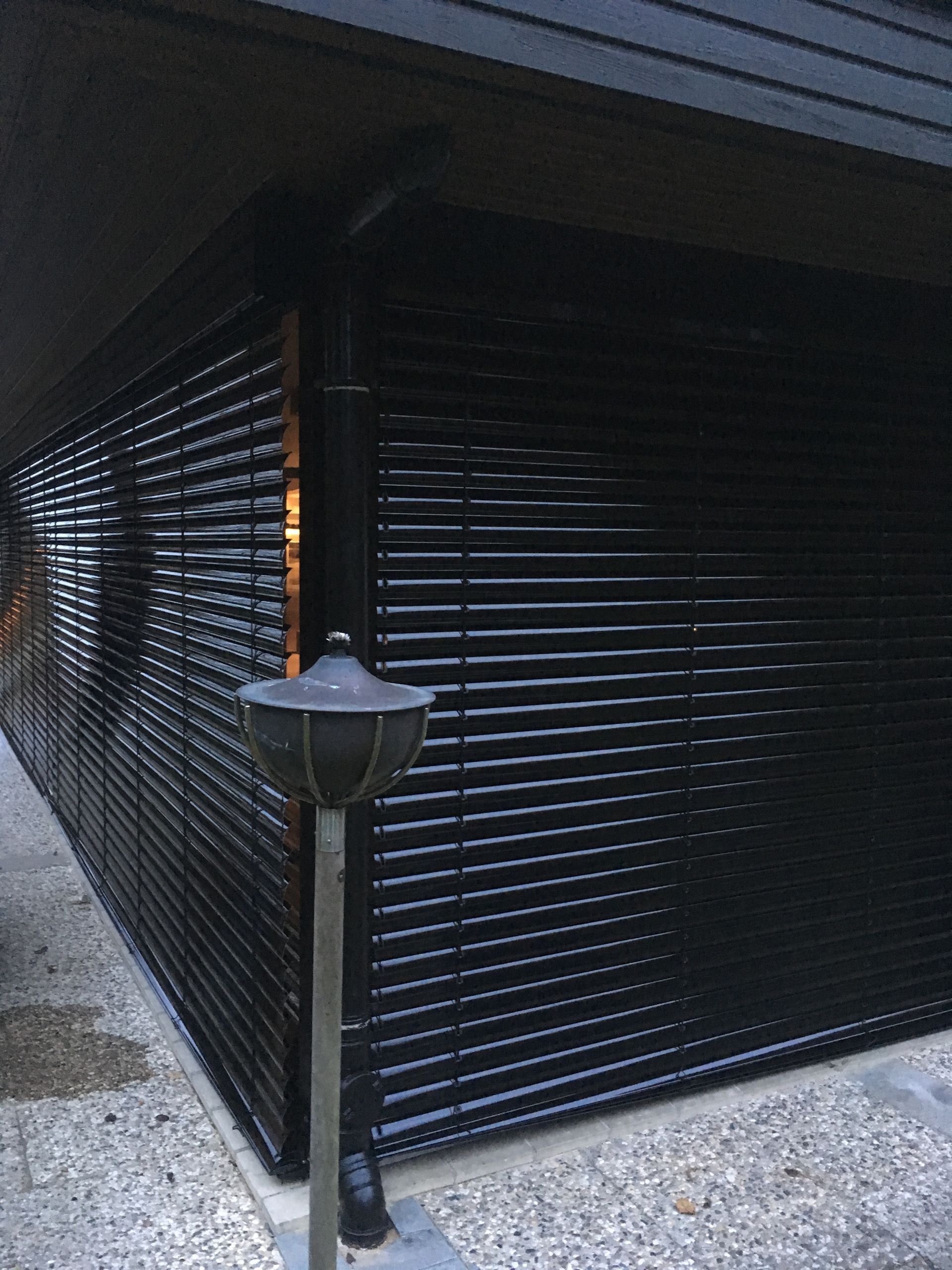 Graue Raffstore auf einer Terrasse mit Blick auf einen Garten mit grünem Laub.