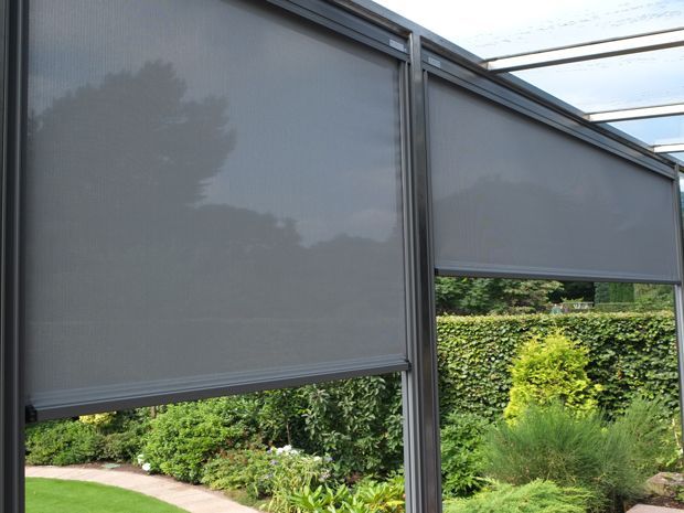 Graue Rollos auf einer Terrasse mit Blick auf einen Garten mit grünem Laub.