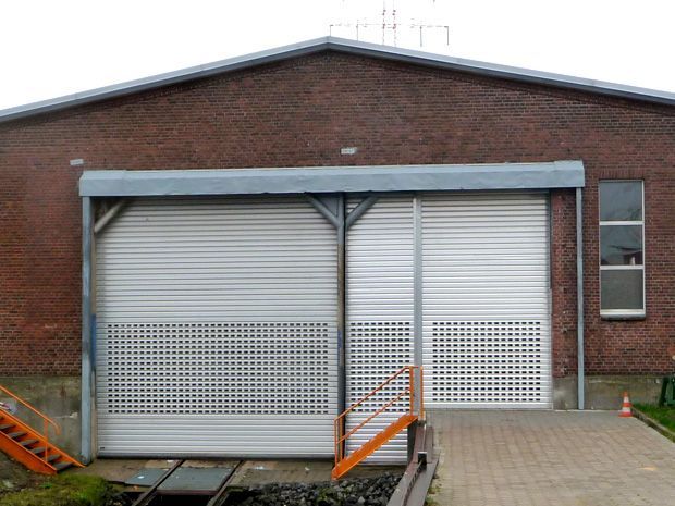 Backsteingebäude mit zwei großen, aufrollbaren Metalltoren, einer Rampe und einem kleinen Fenster.