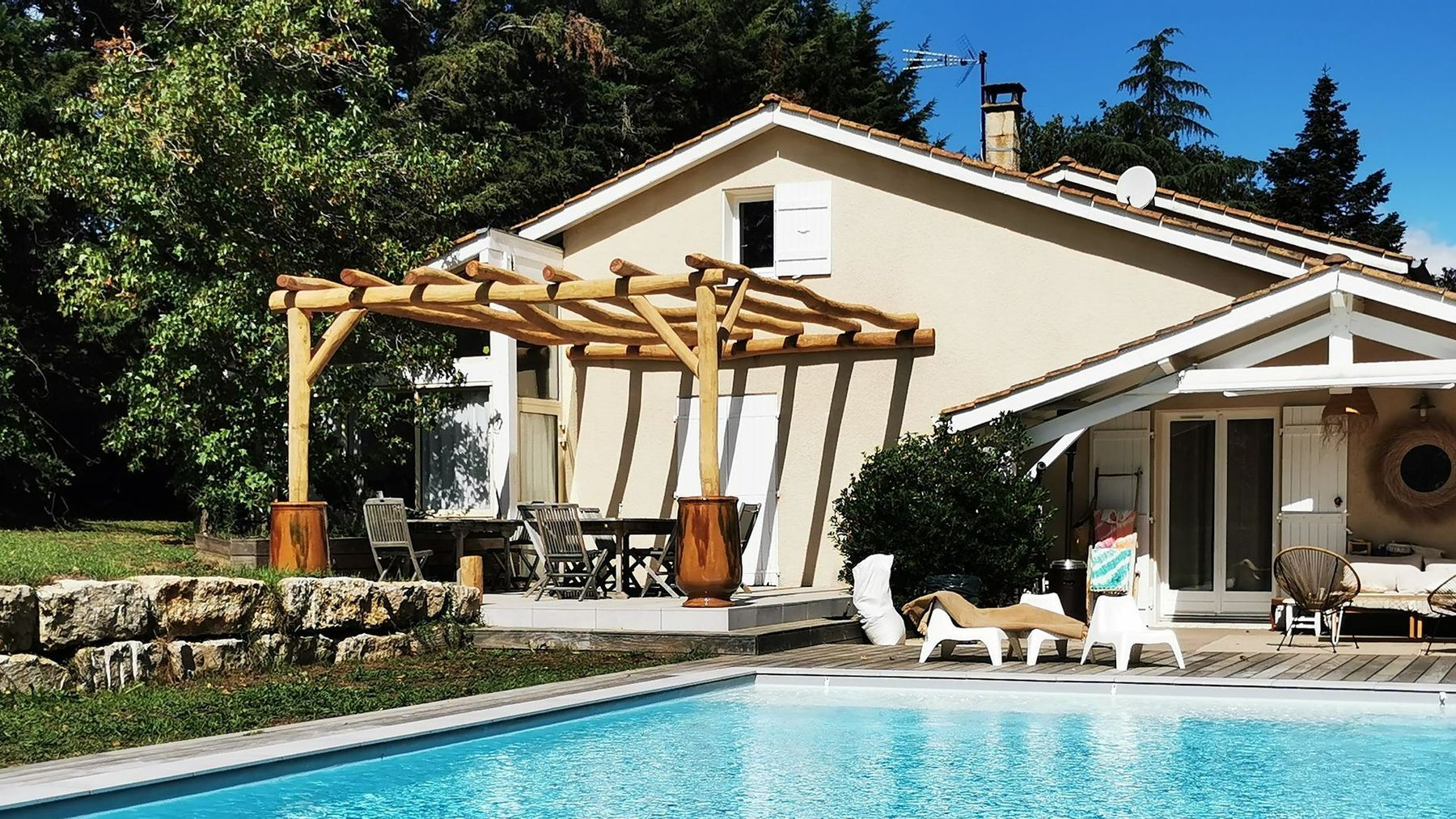 Piscine et pergola en bois devant une maison blanche