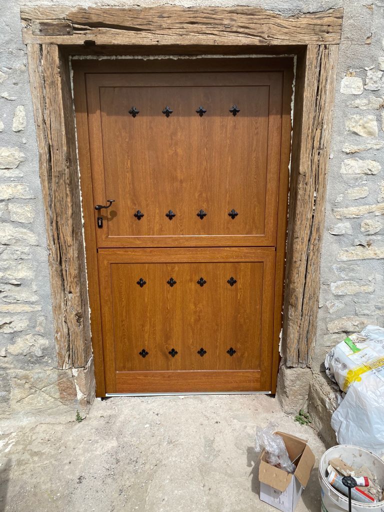 Una puerta de madera estilo establo con remaches decorativos de metal negro, enmarcada en piedra y colocada sobre una pared de piedra tosca.
