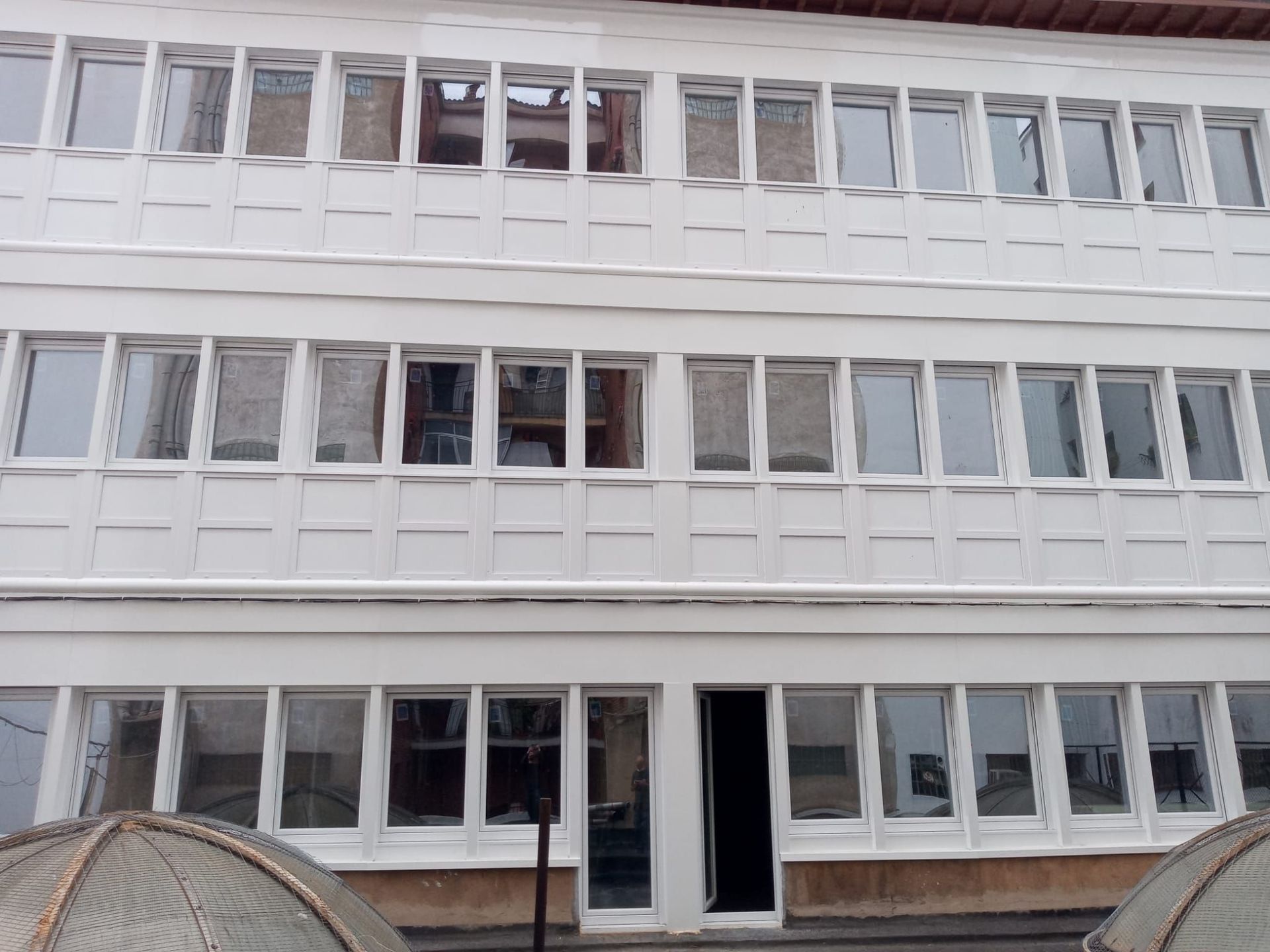 Un edificio blanco de tres plantas con hileras de ventanas rectangulares idénticas y una entrada oscura en la planta baja.