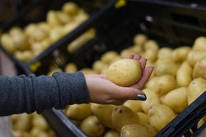 Mano sosteniendo una papa de un contenedor de papas en una tienda de comestibles.