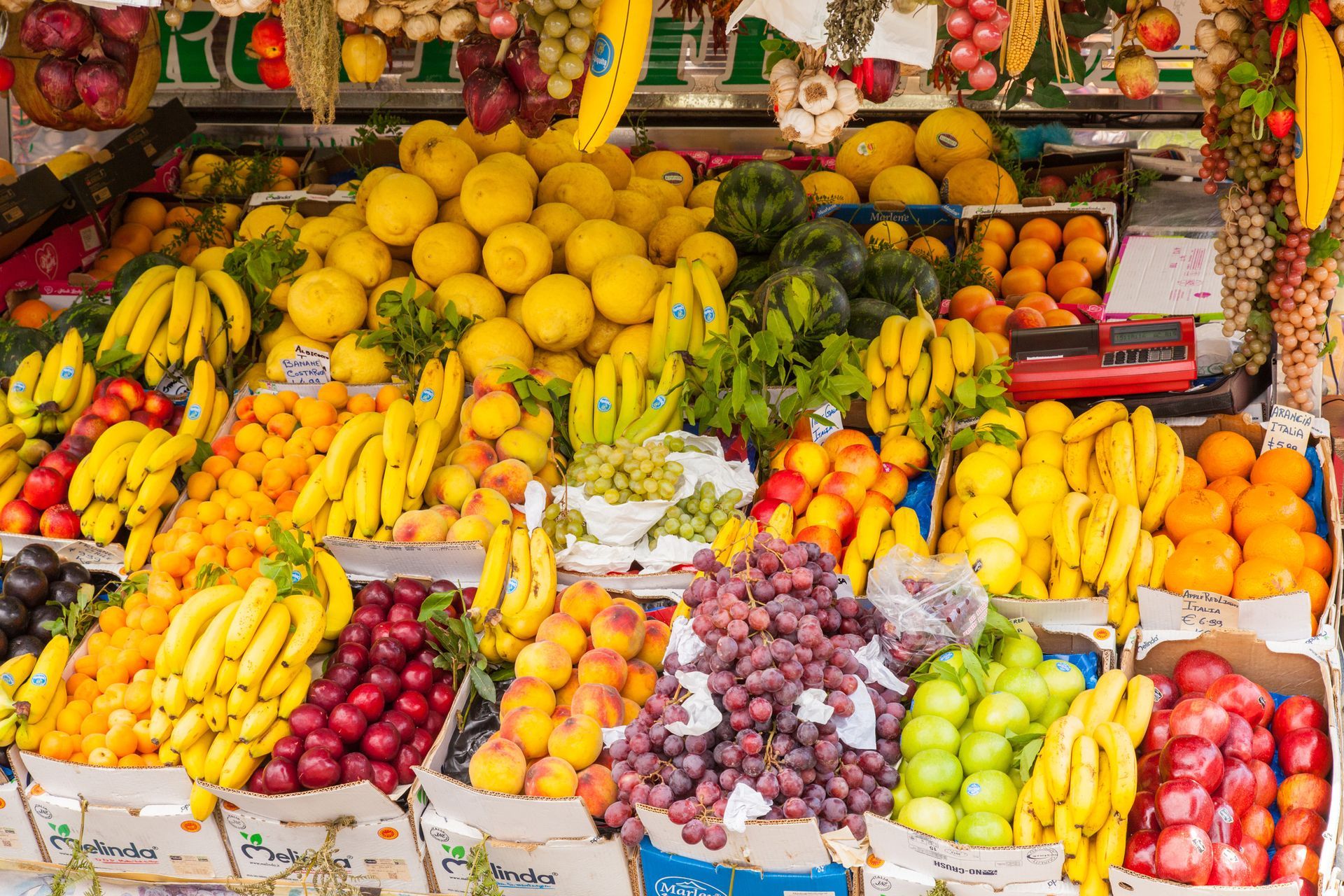 Exhibición de frutas: plátanos, limones, naranjas, uvas y otros productos en varios colores.