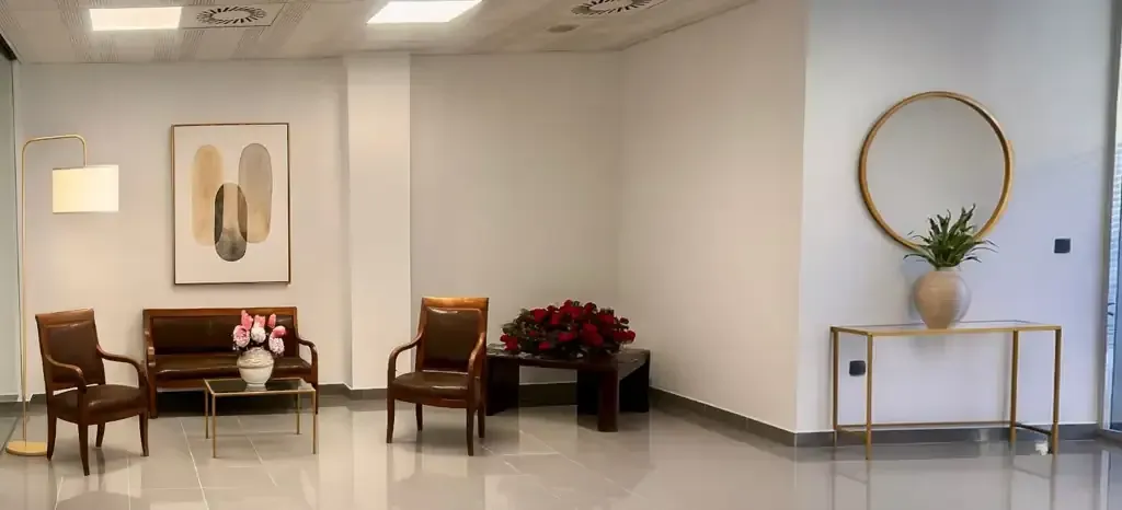 Una elegante sala de espera con asientos, obras de arte, flores y un espejo con marco dorado. 