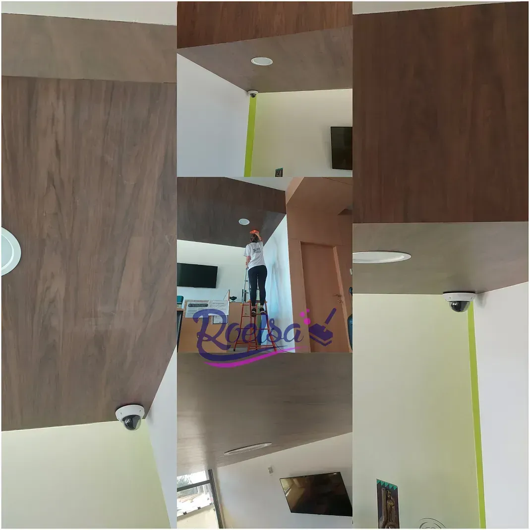 Un hombre está de pie en una escalera en una sala de estar limpiando el techo.