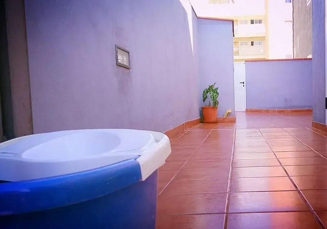 Un bote de basura azul está sobre un piso de baldosas en un pasillo.