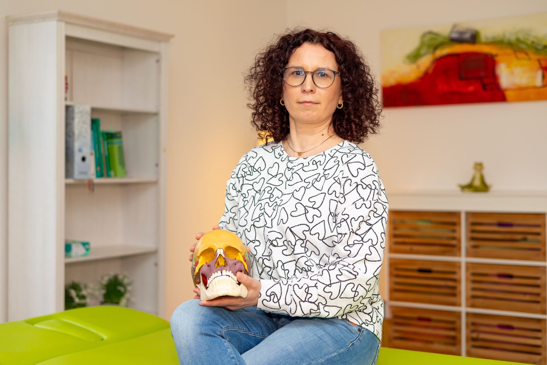 Eine Frau sitzt auf einem grünen Tisch und hält einen Totenkopf.