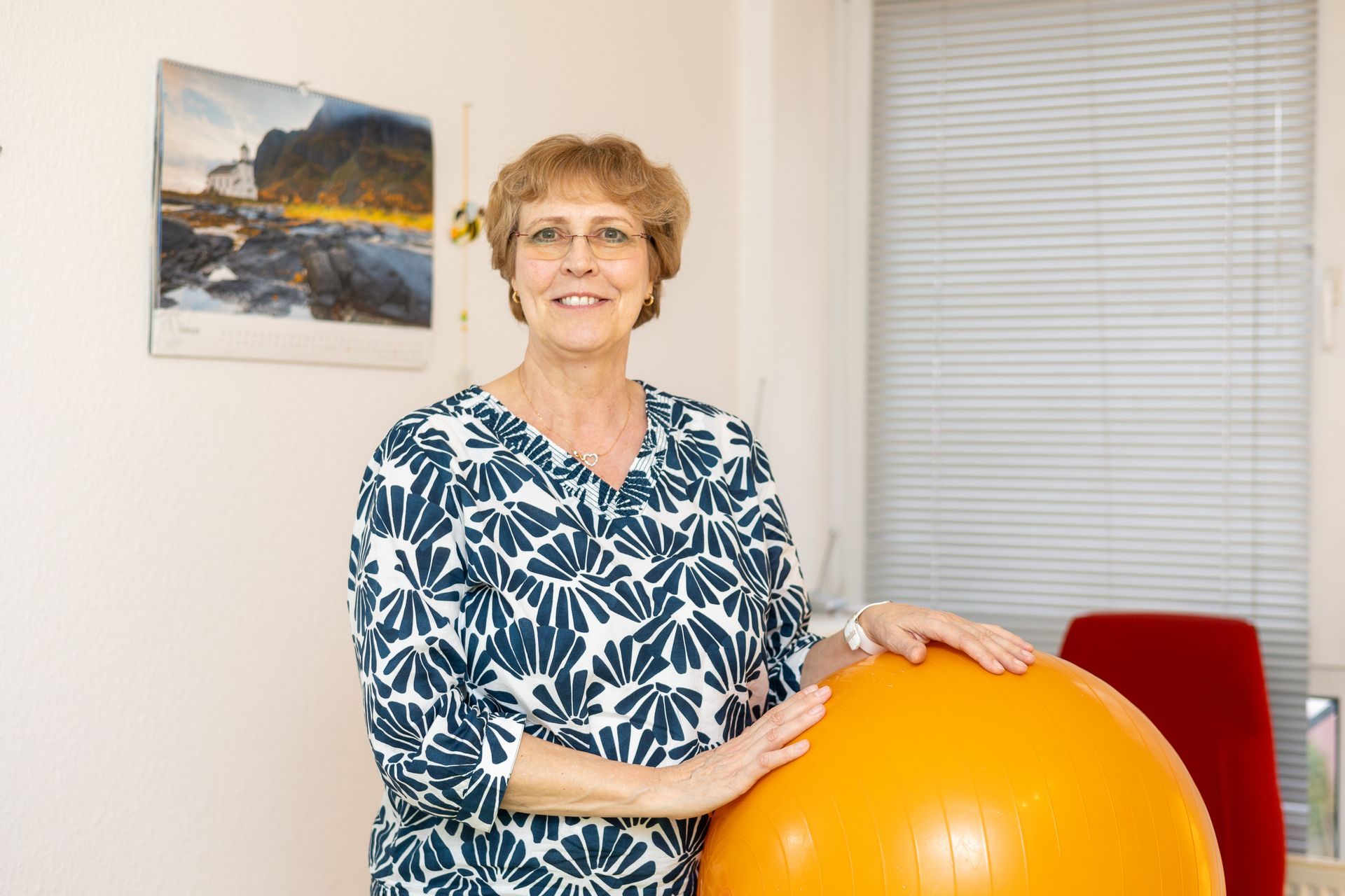 Eine Frau hält in einem Raum einen orangefarbenen Gymnastikball.