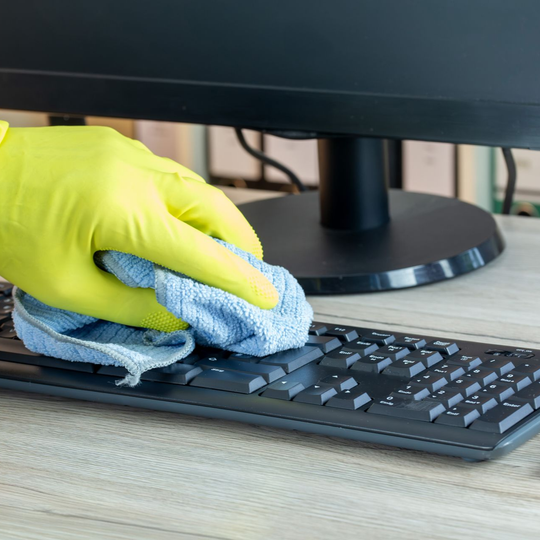 Une personne portant des gants jaunes nettoie un clavier d'ordinateur avec un chiffon bleu.