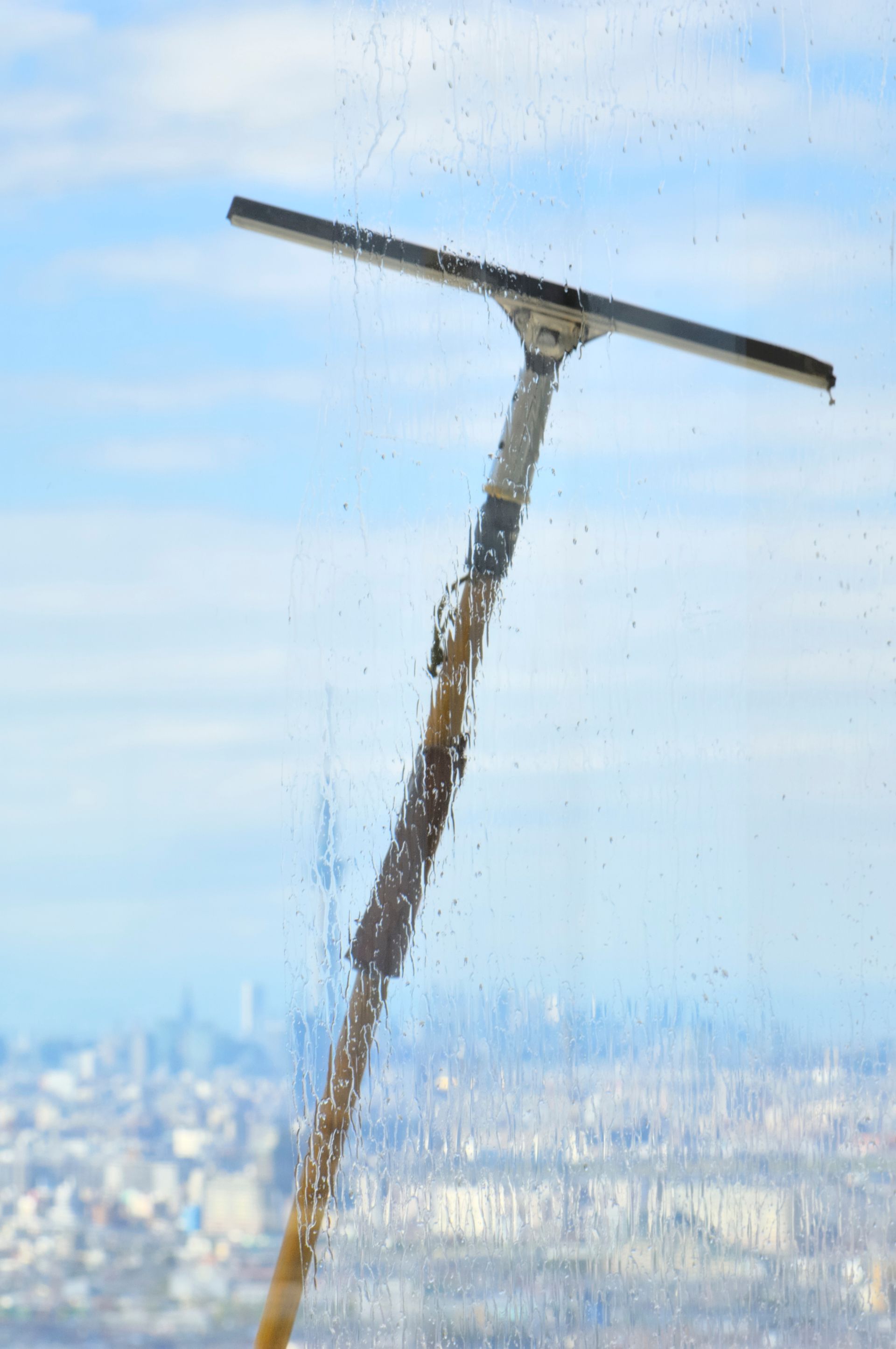 Une raclette nettoie une vitre laissant apparaître la silhouette de la ville à travers le verre.