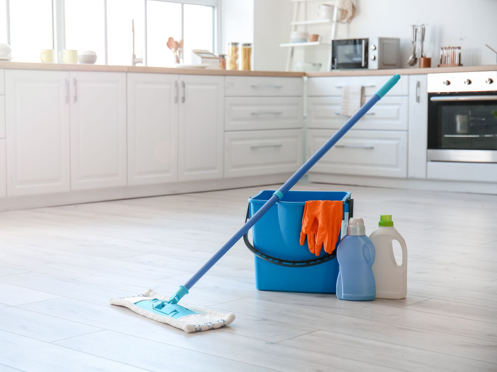 Matériel de nettoyage pour le sol de la cuisine : balai-serpillière, seau, gants et produits de nettoyage.