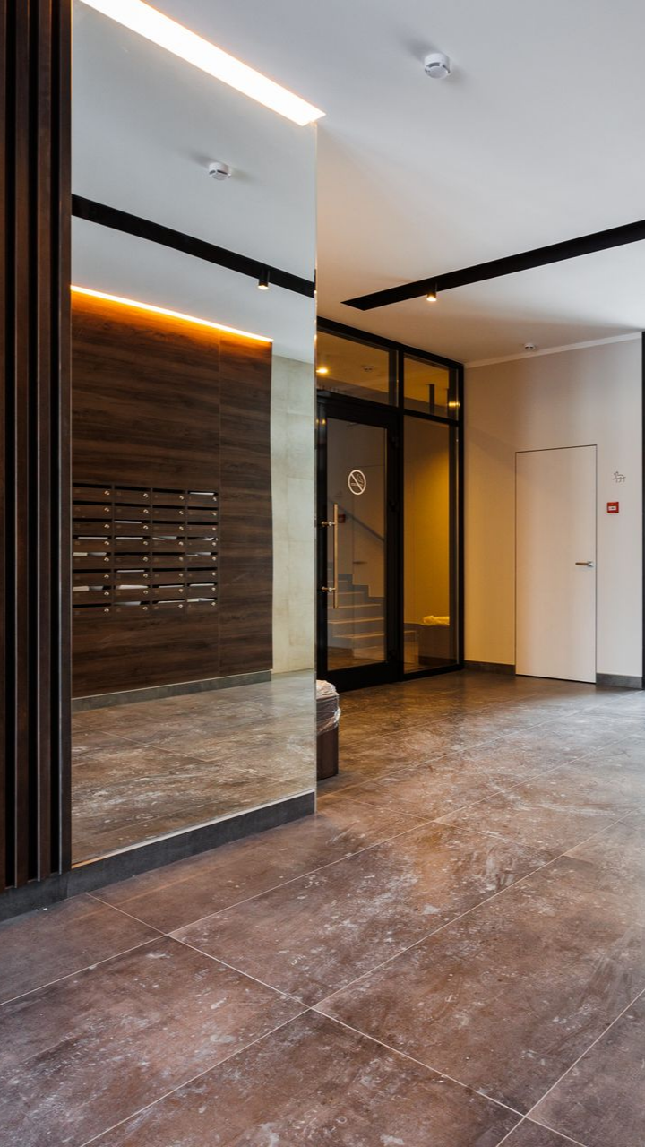 Entrée d'un immeuble d'appartements moderne avec un grand miroir, des boîtes aux lettres et une porte vitrée.