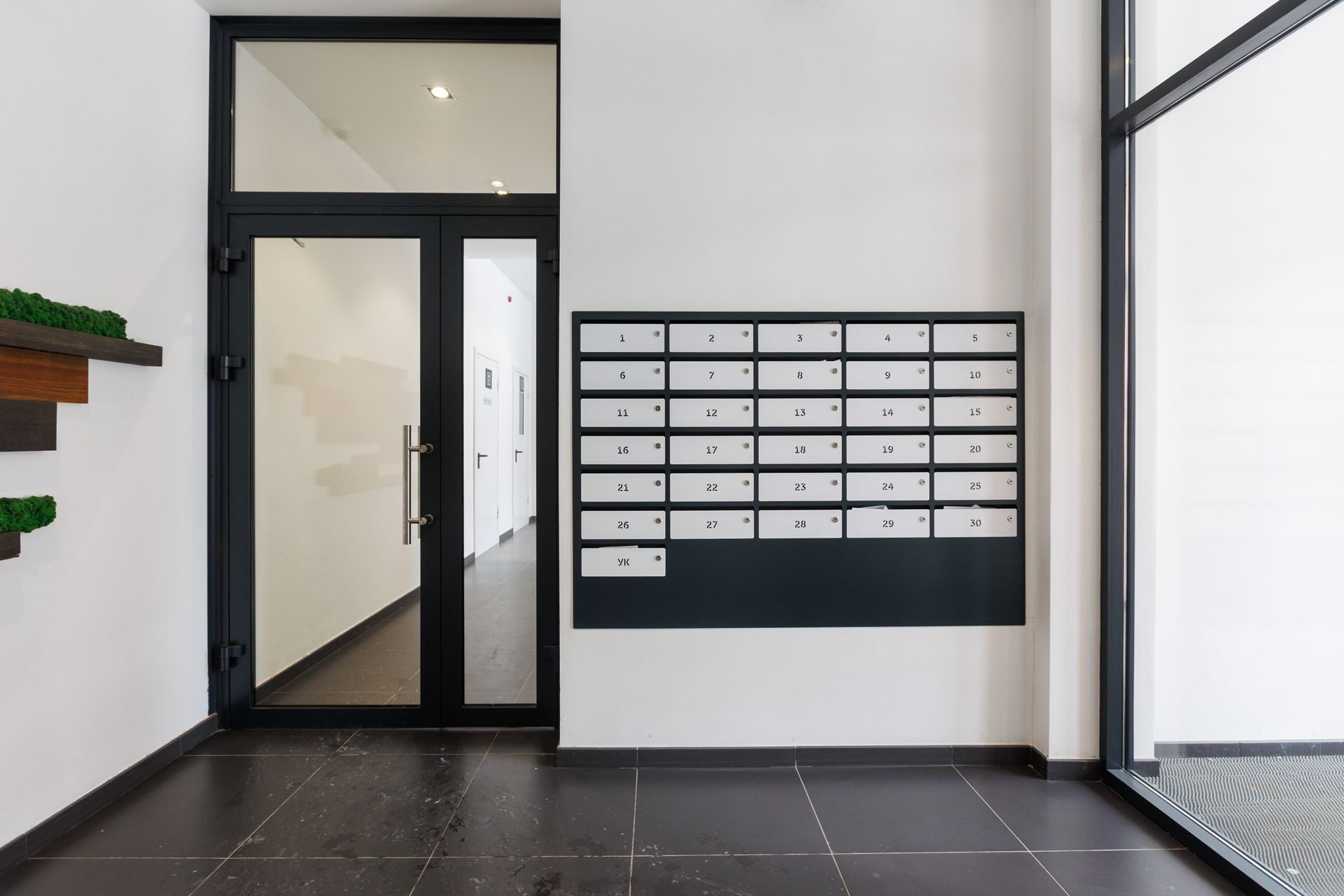 Boîtes aux lettres dans une entrée avec porte vitrée et grande fenêtre.
