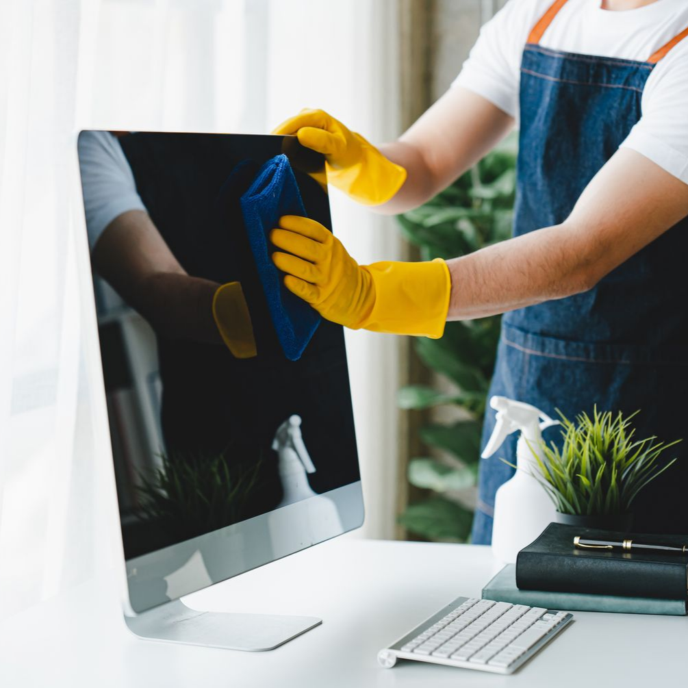 Une personne nettoie un écran d'ordinateur avec un chiffon bleu, portant des gants jaunes et un tablier.