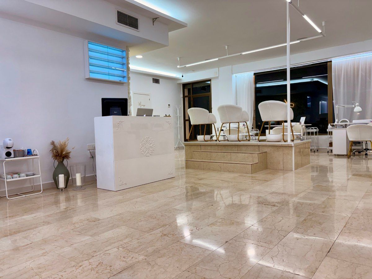Interior de un salón de uñas con mostrador de recepción, estaciones de manicura y sillas de pedicura.