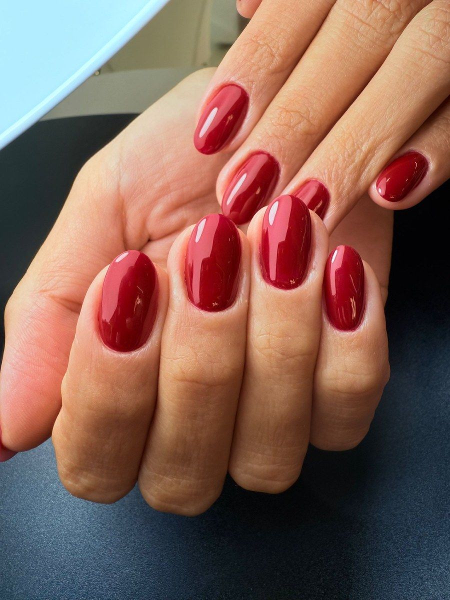Manos con uñas de forma ovalada pintadas de un rojo oscuro brillante.