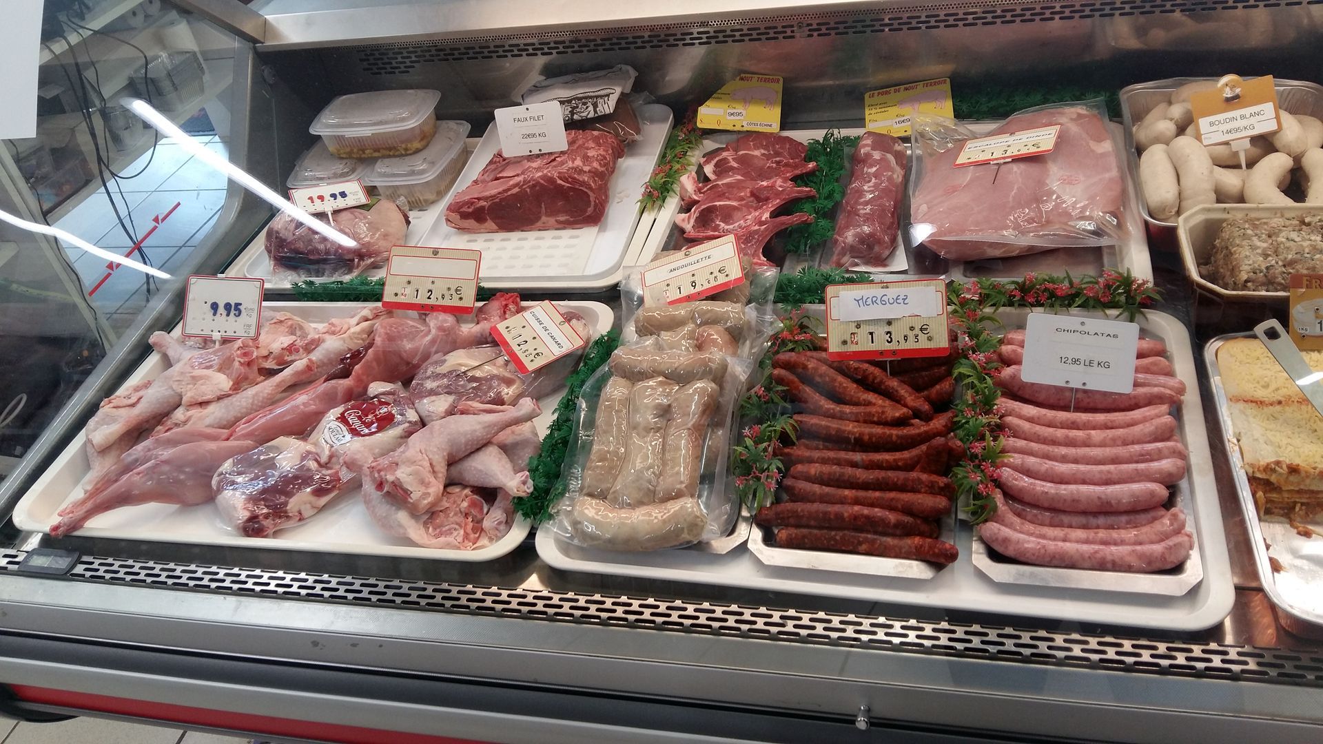 Vitrine de boucherie avec viandes tranchées, saucisses et poulet.