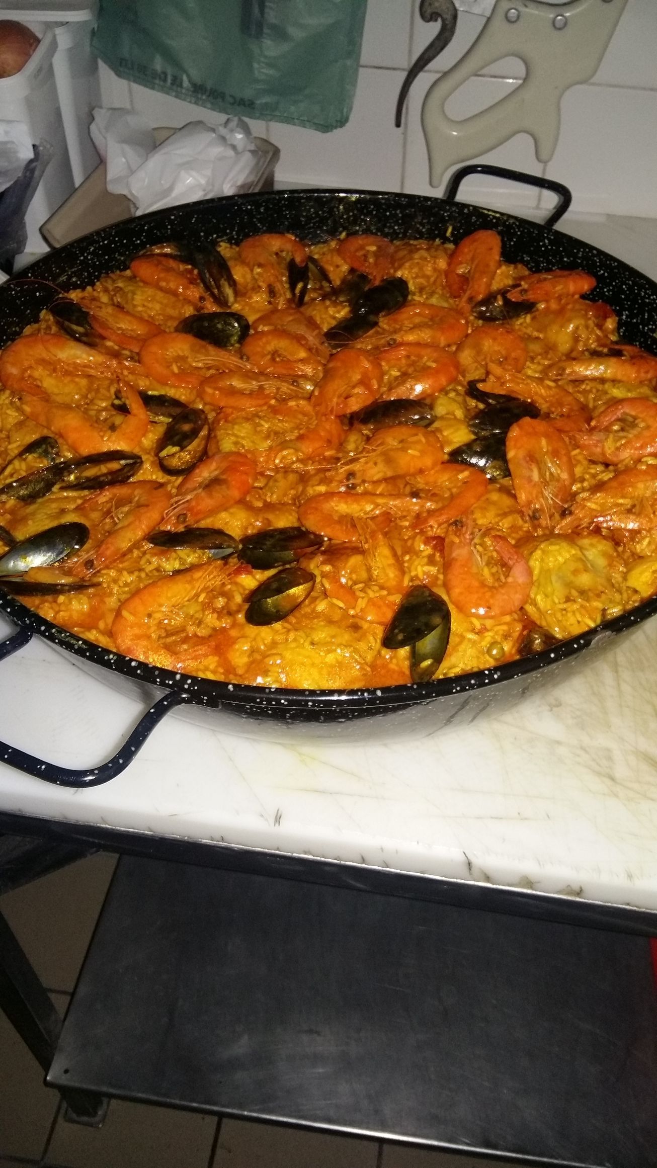 Grande poêle à paella remplie de fruits de mer, notamment de crevettes et de moules, posée sur une cuisinière.