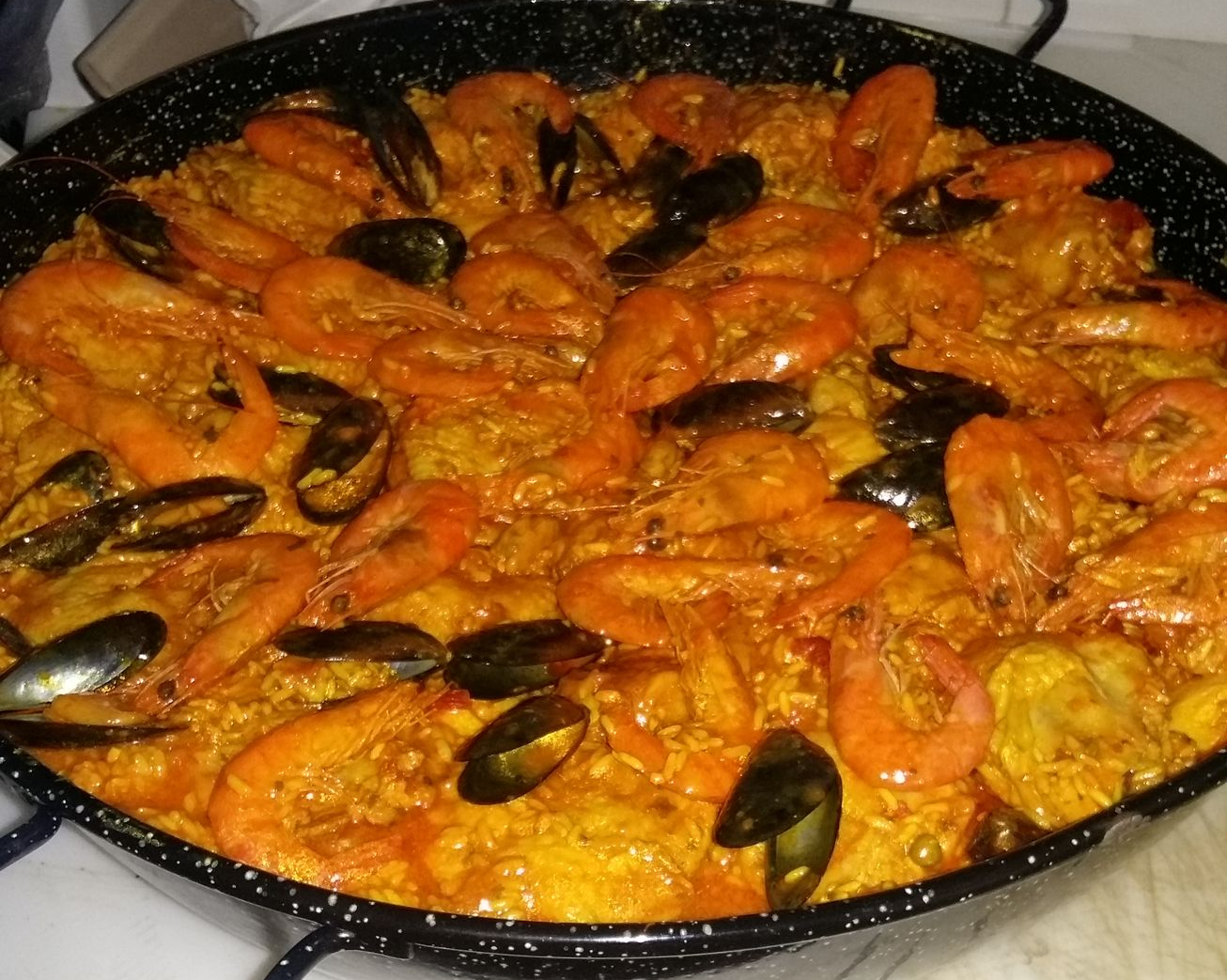 Paella dans une grande poêle noire, composée de crevettes, de moules et de riz jaune.