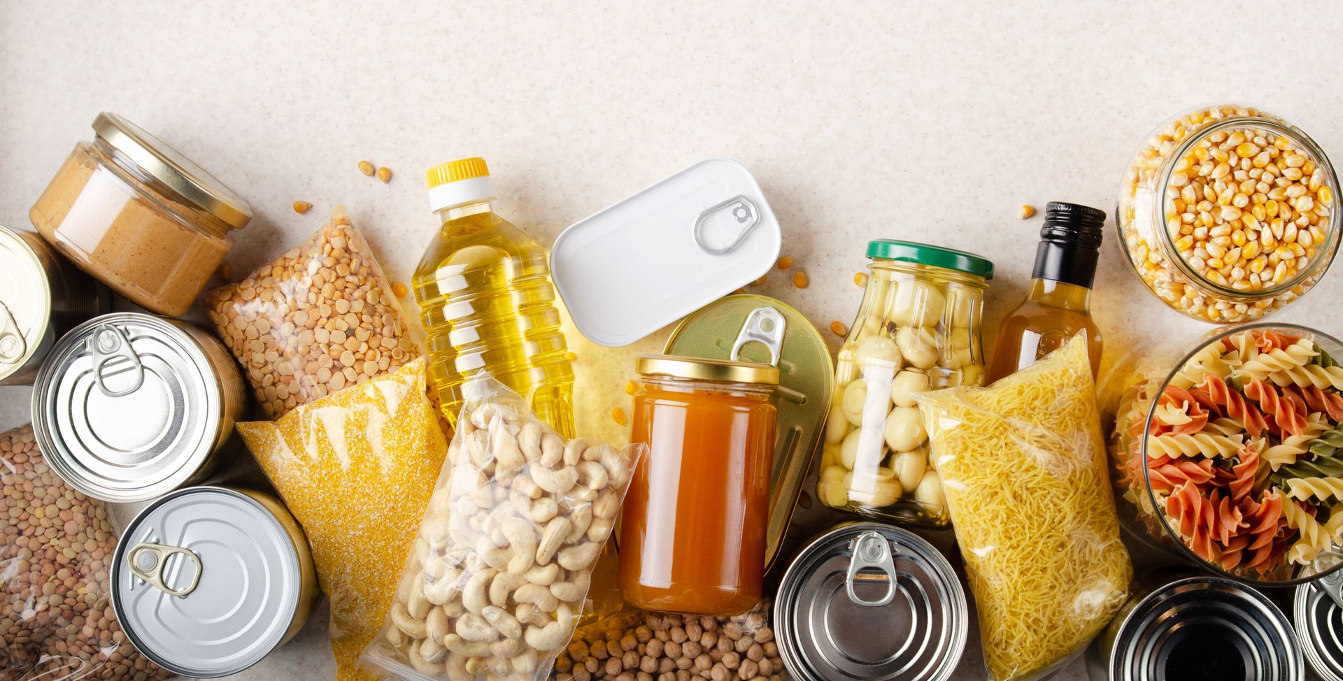 Divers produits alimentaires non périssables : conserves, bocaux, pâtes, huile, haricots. Fond blanc.