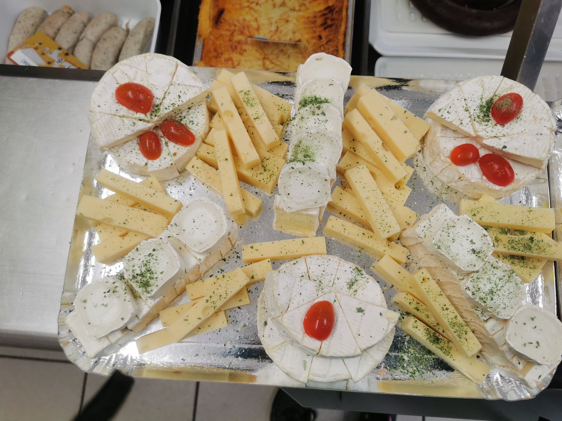 Plateau de fromages avec divers fromages, tomates cerises et herbes.