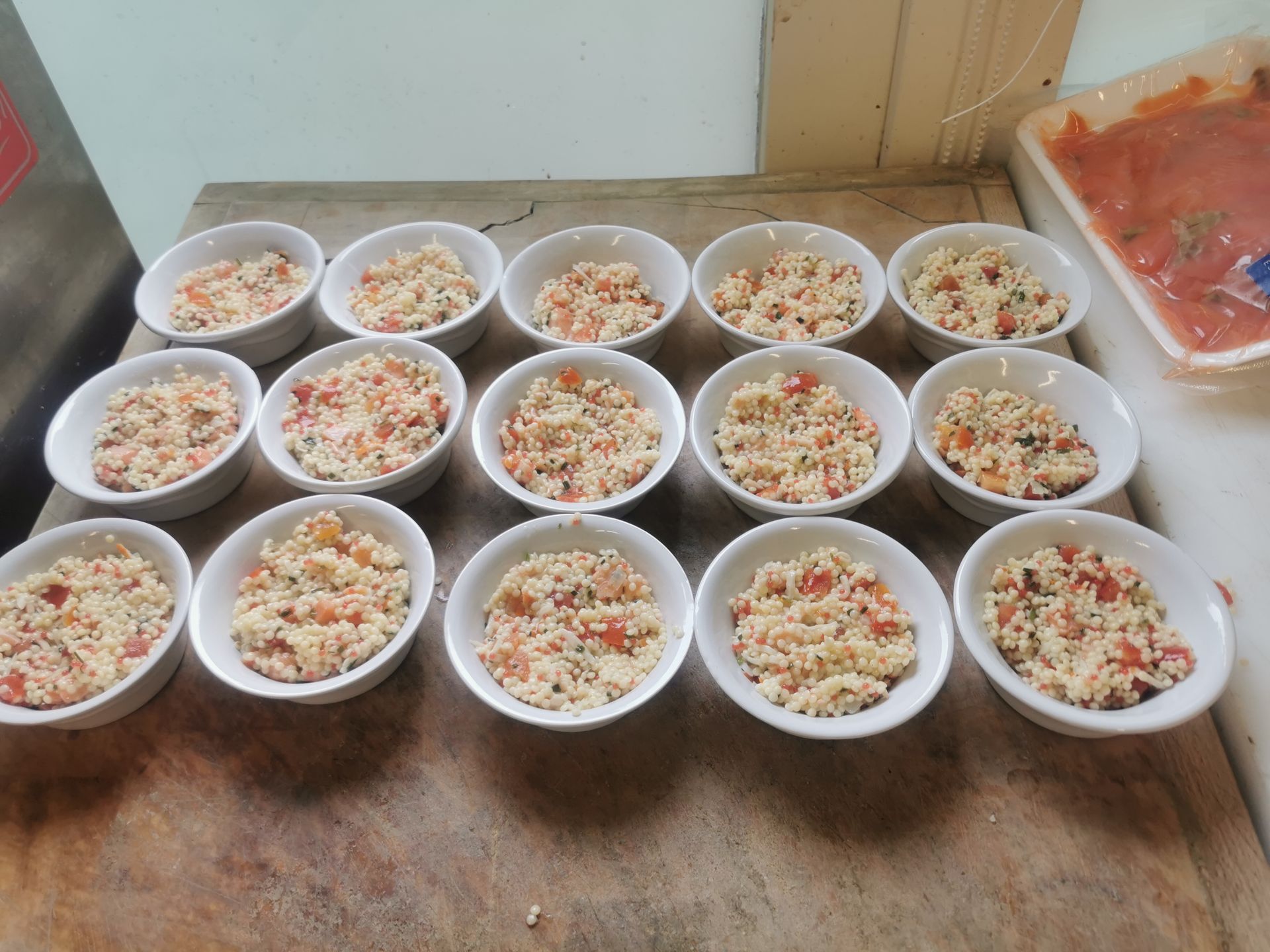 Quinze bols blancs remplis d'un mélange de couscous coloré sur une surface en bois.