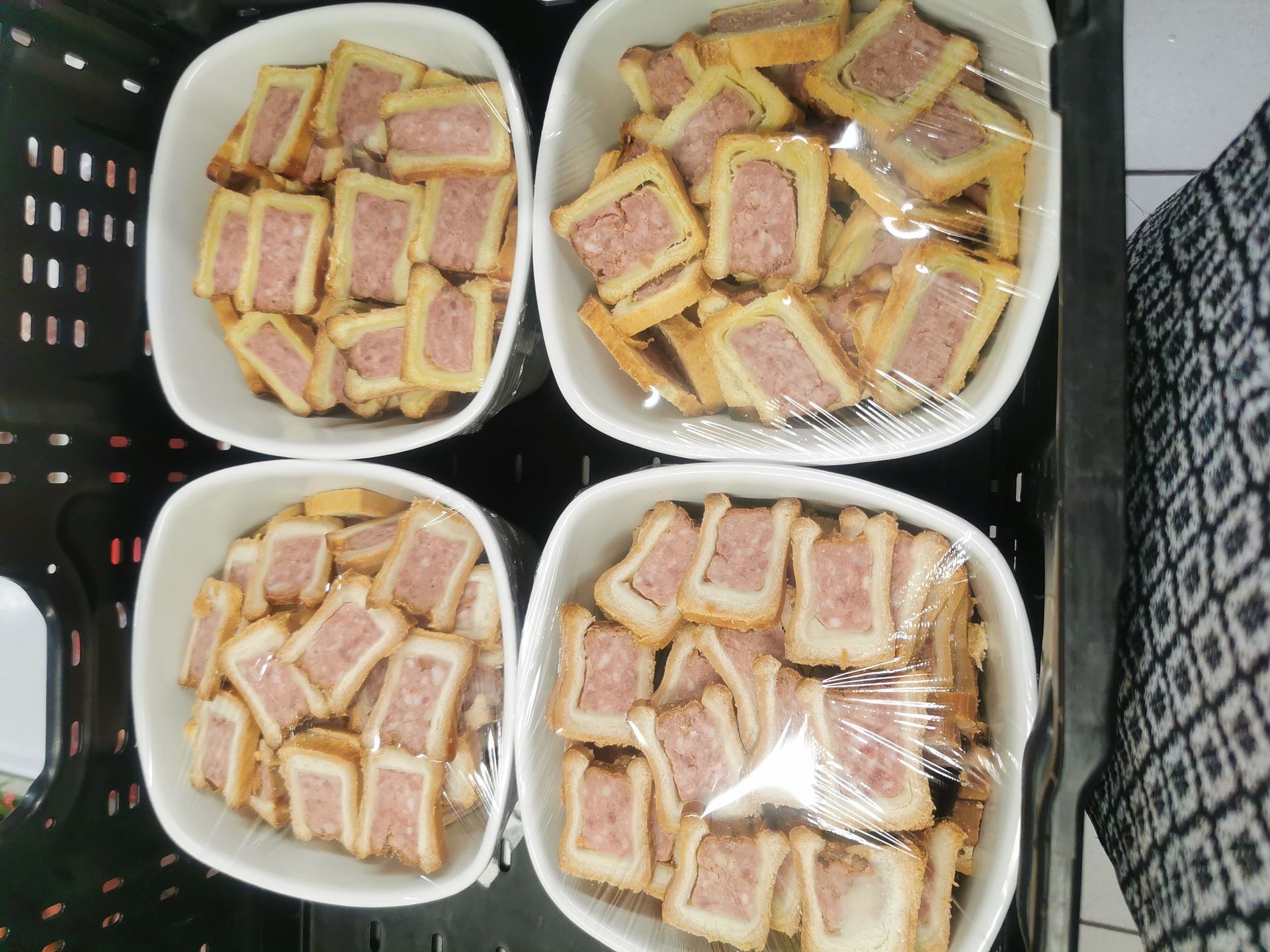 Quatre contenants blancs contenant des sandwichs rectangulaires avec une garniture rose, recouverts d'une pellicule plastique.