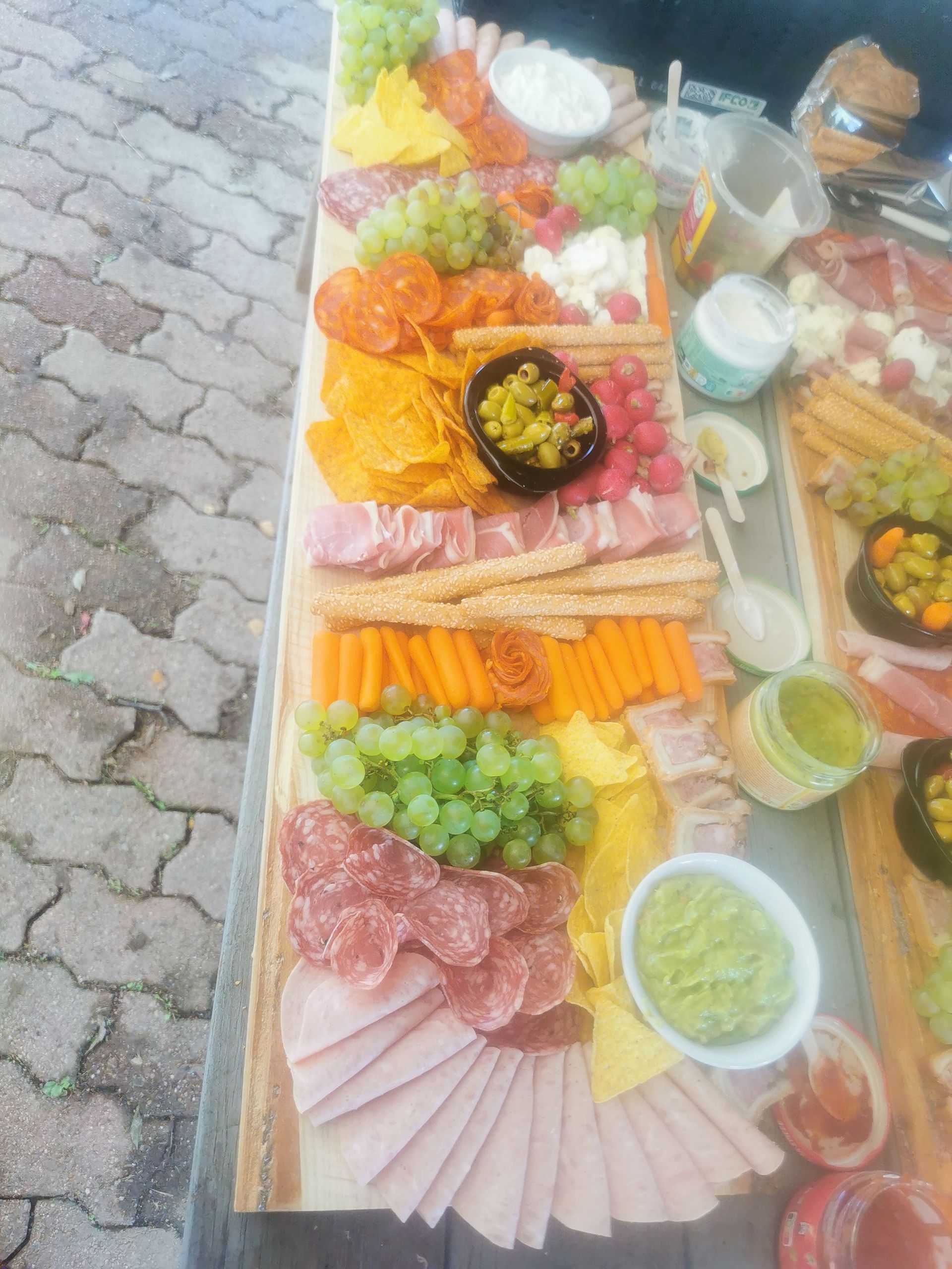 Planche de charcuterie avec viandes, fromages, fruits et trempettes disposés sur une surface en bois.