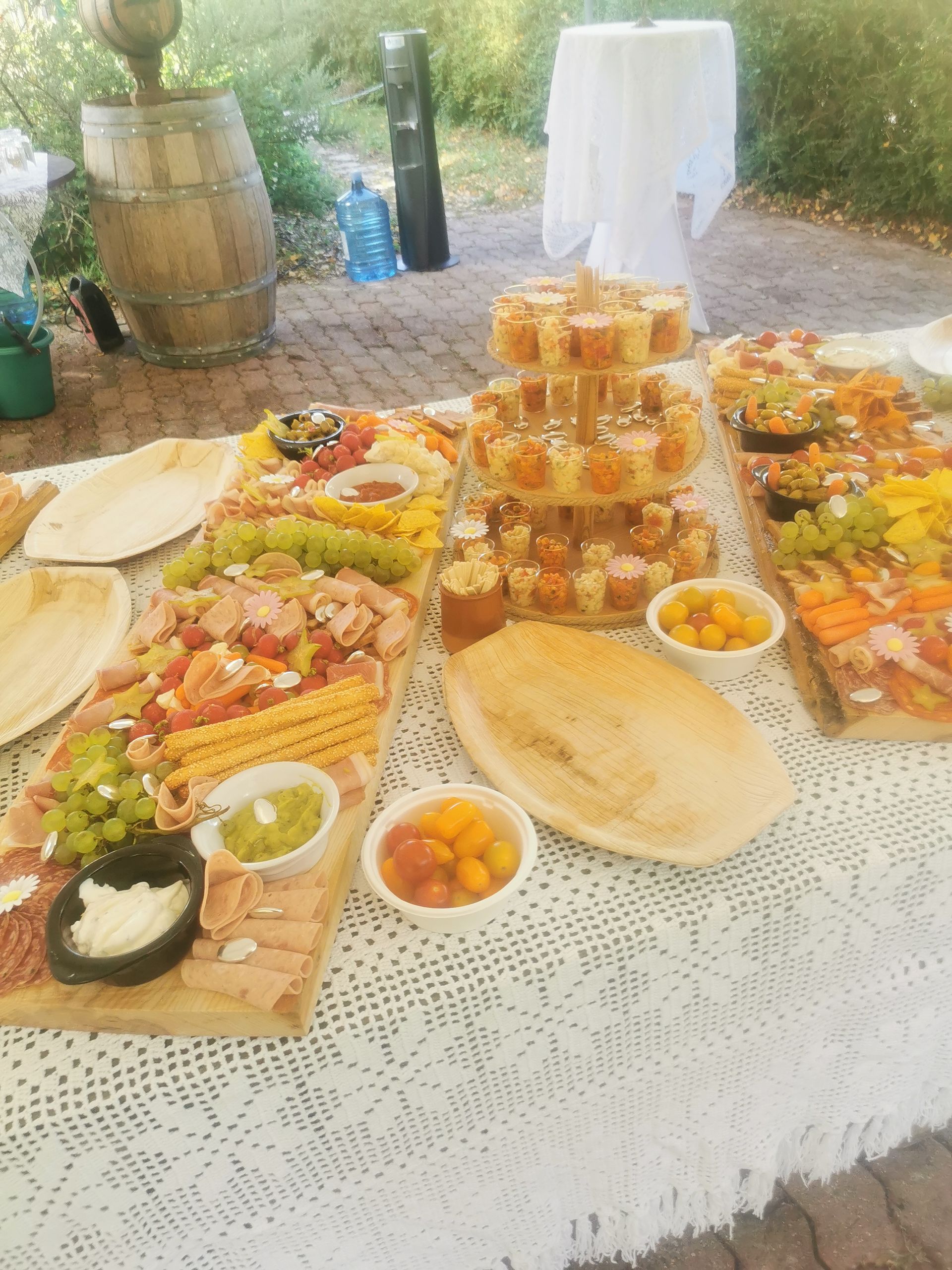 Une table avec charcuterie, entrées et desserts pour un événement en plein air, avec un tonneau en arrière-plan.