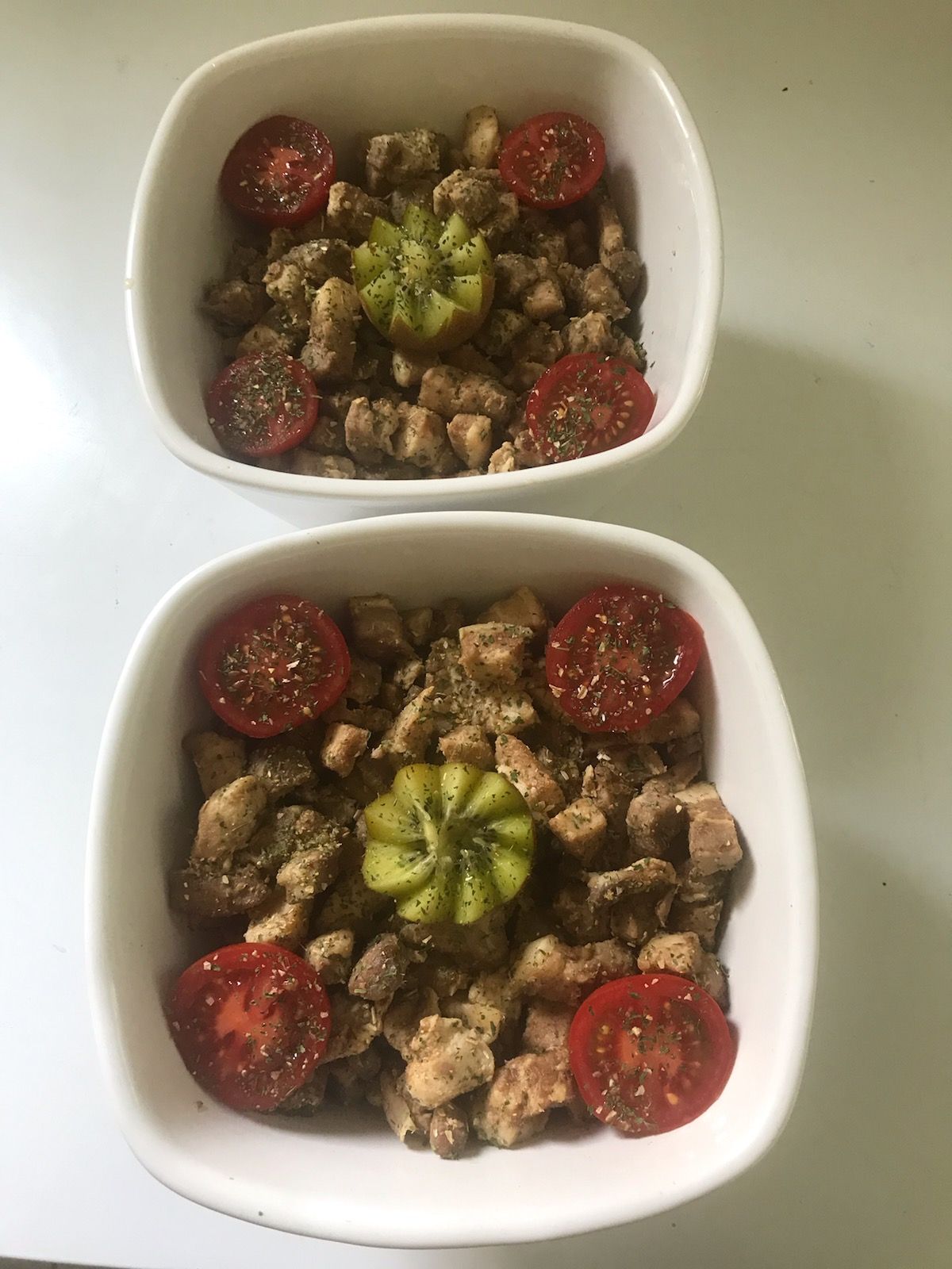 Deux bols blancs avec du poulet, des tomates et un poivron vert.