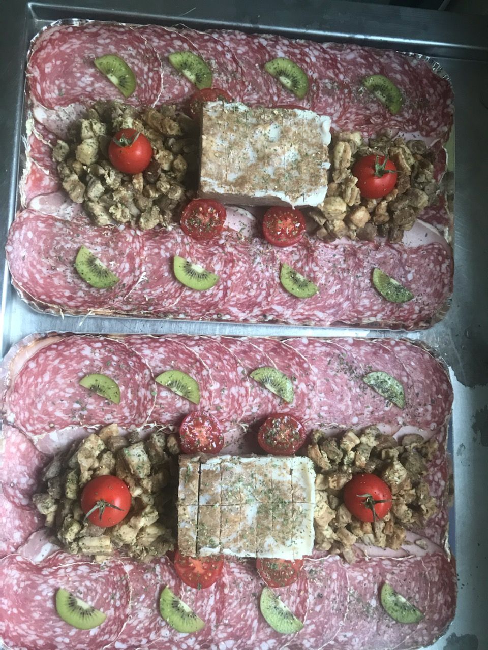 Deux plateaux de charcuterie rectangulaires avec salami, kiwi, croûtons, tomates et fromage.