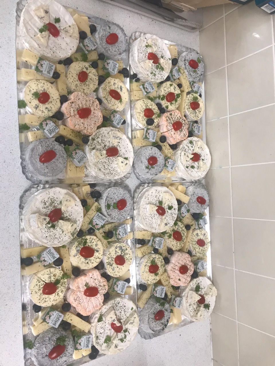 Quatre plateaux de nourriture avec fromages, garnis, sur un comptoir blanc.