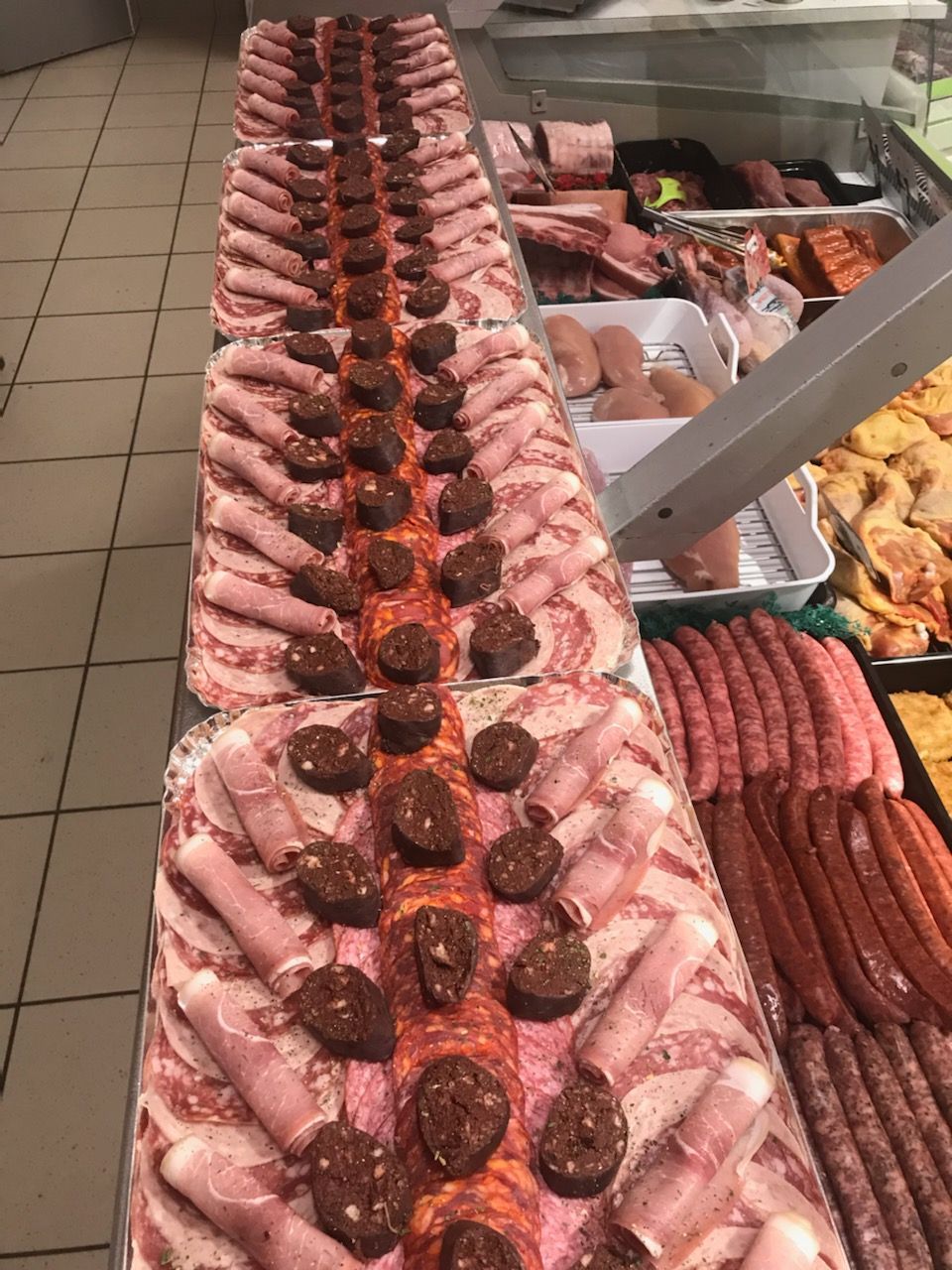 Disposition de viandes tranchées et de saucisses dans un présentoir de boucherie, couleurs et textures variées.