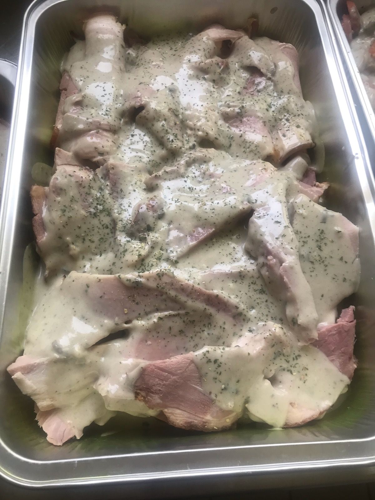 Tranches de jambon dans une poêle en métal, recouvertes de sauce crémeuse aux herbes vertes.