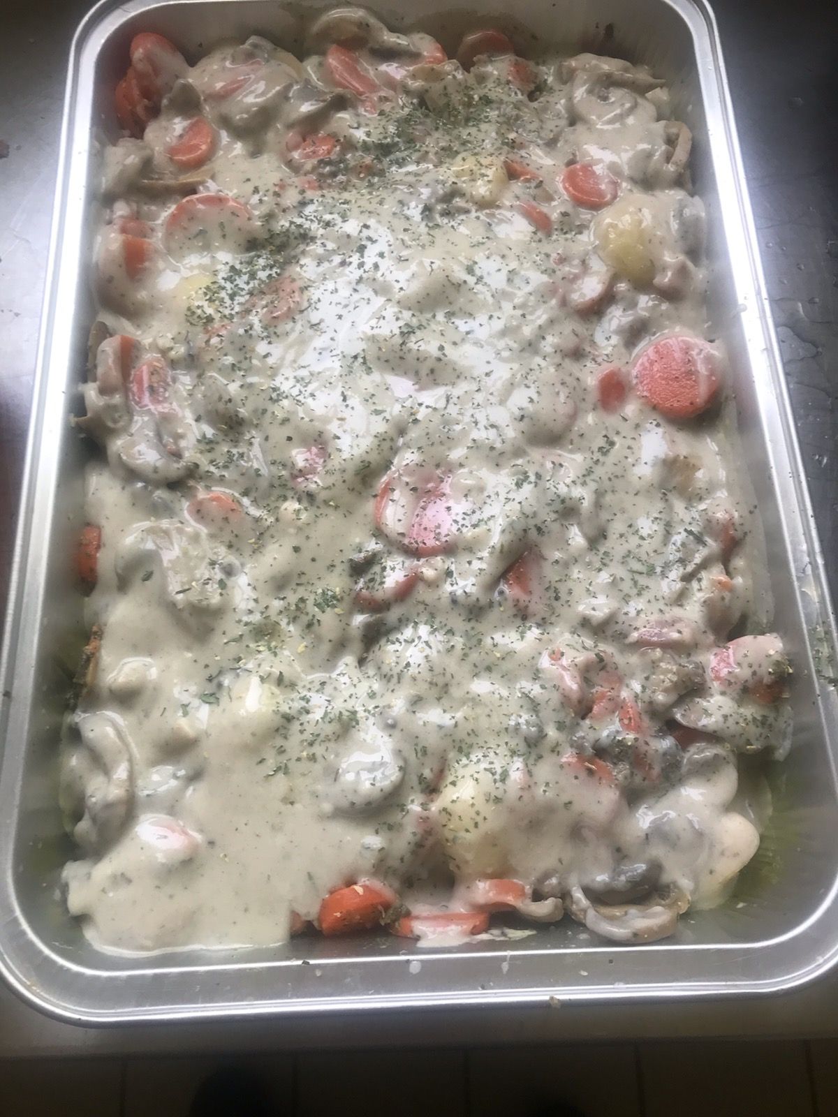 Cocotte dans une poêle en métal, avec carottes et sauce crémeuse, saupoudrée d'herbes.