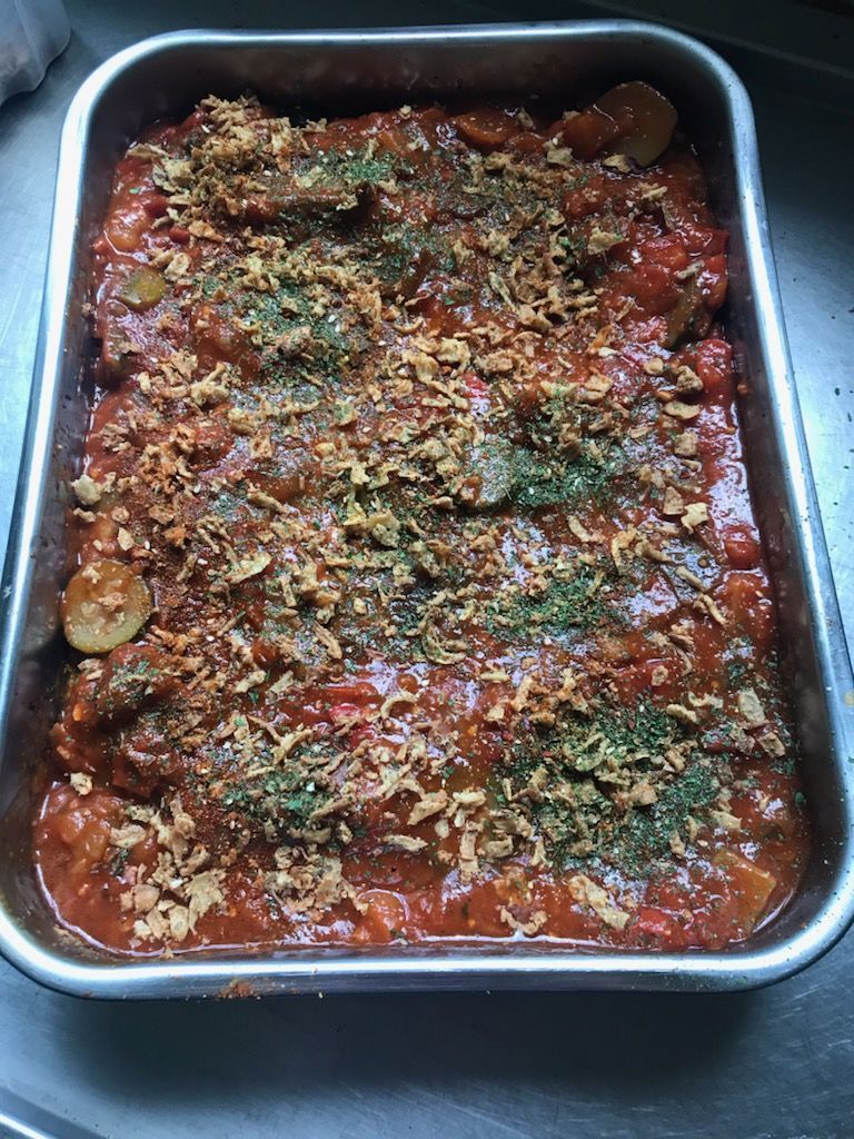 Plat cuit au four dans une poêle en métal, sauce rouge avec garniture d'herbes et chapelure brune.